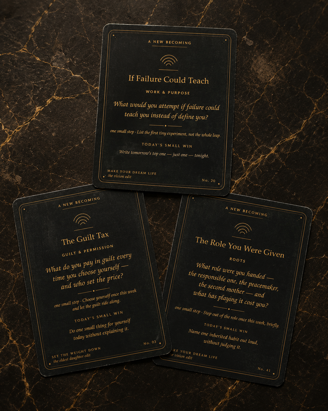 Three A New Becoming cards fanned on dark marble